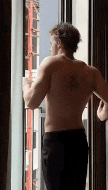 a shirtless man is standing in front of a window in a room .