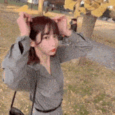 a woman is standing in front of a tree holding her hair .