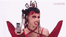 a woman in a red dress is sticking her tongue out and holding a cell phone in front of an emoji that says glamour