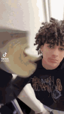 a young man with curly hair is sitting at a table in a room .