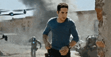a man in a blue shirt is running through a destroyed city with a drone flying in the background .