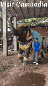 a man standing next to a decorated elephant that says visit cambodia on it