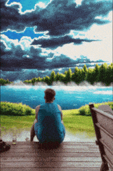 a man in a blue tank top sits on a deck looking out over a lake