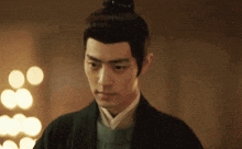 a man with a bun on his head is standing in a dark room with lights behind him .