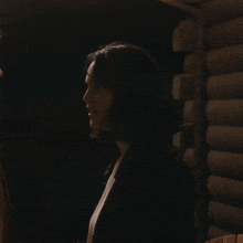 a woman is sitting in a dark room with a wooden wall behind her