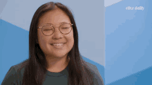 a woman wearing glasses is smiling in front of a blue wall with elite daily written on it