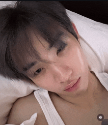 a man in a white tank top is laying on a bed with his eyes closed