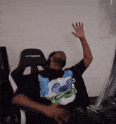 a man sitting in a gtracing chair with his hand up in the air