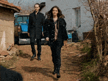 a man and a woman walk down a dirt road