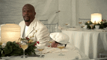 a man in a white suit sits at a table