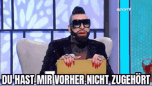 a man with a beard and sunglasses is sitting in a chair holding a box .