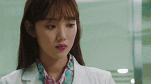 a woman wearing a white coat and a floral scarf is looking at the camera .