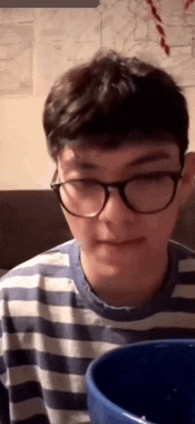 a young boy wearing glasses and a striped shirt is looking at a blue bowl .