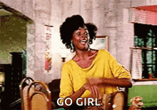 a woman in a yellow shirt is sitting at a table and says go girl