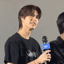 a man wearing a black shirt with the word swans on it holds a microphone