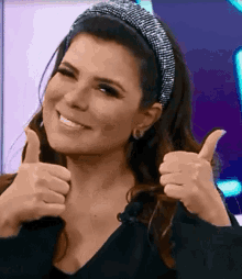 a woman wearing a headband is smiling and giving two thumbs up