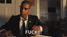 a man in a suit and tie is sitting at a desk with a book in his hand .
