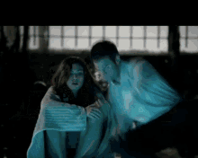 a man and a woman are sitting under a blanket in the dark