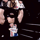 a man in a john cena shirt holds up a wrestling belt