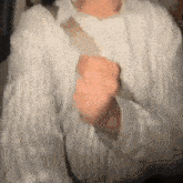 a person wearing a white sweater is holding something in their hand