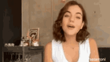 a woman in a white tank top is standing in front of a bar ..