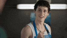 a young man wearing a white tank top and blue overalls smiles