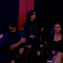 a man and two women are sitting in a dark room with a red curtain behind them