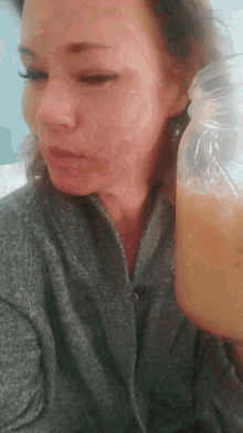 a woman in a grey sweater is holding a plastic bottle