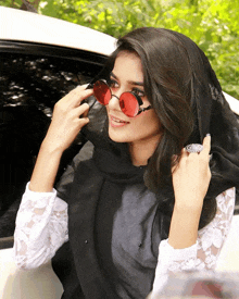 a woman wearing a scarf and red sunglasses is standing in front of a car