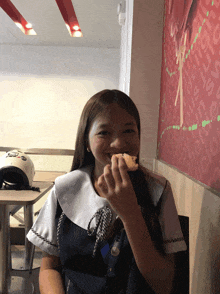 a girl is eating a piece of food in front of a wall that says delicious