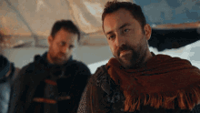 a man with a scarf around his neck is standing next to another man with a beard