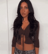 a woman in a brown crop top and jeans is standing in front of a white wall