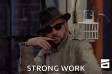 a man wearing sunglasses and a hat is sitting at a table and says strong work