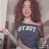 a woman with curly hair is wearing a blue crop top and a white bracelet .