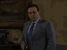 a man in a suit and tie is holding a glass of wine while standing in a living room .