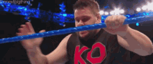a man in a black shirt with the word ko on it is holding a blue rope in his mouth .