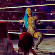 a woman with blue hair is dancing in a wrestling ring with a crowd watching .