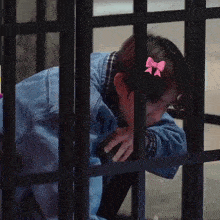 a girl with a pink bow in her hair looks through bars