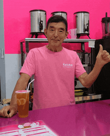 a man wearing a pink shirt that says koicha on it gives a thumbs up