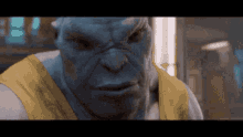 a close up of a blue monster wearing a yellow shirt and looking at the camera .