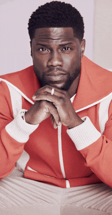 a man wearing a red and white jacket has his hands folded in front of his face