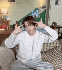 a man is sitting on a couch making a peace sign with his hands .
