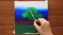 a person is painting a picture of a mountain with green paint