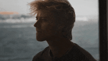 a young man looking out a window with his hair blowing