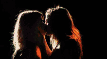 two women are kissing in the dark in front of a black background .