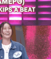a woman in a denim jacket is smiling in front of a sign that says " kips a beat "