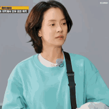 a woman wearing a blue sweatshirt with a black strap looks at the camera