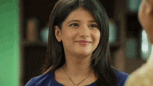 a woman wearing a blue shirt and a necklace is smiling while looking at a man .