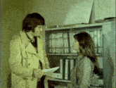 a man is giving a piece of paper to a woman in front of a shelf full of binders