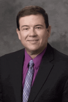 a man in a suit and purple shirt is smiling
